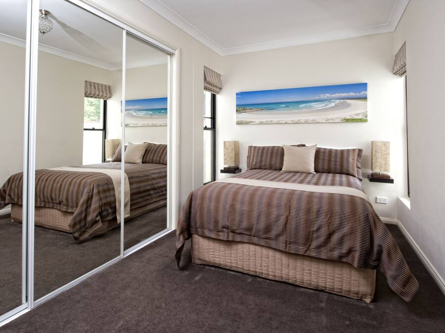 Un dormitorio con cama, un espejo grande, un cuadro de playa y una ventana con cortinas.