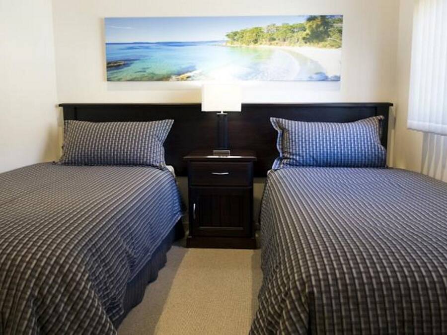 A hotel room with two single beds, a nightstand with a lamp, and a painting of a coastal scene.