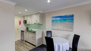 Cocina compacta con microondas, pileta y alacenas, una mesa de comedor con sillas y un cuadro de una playa en la pared.