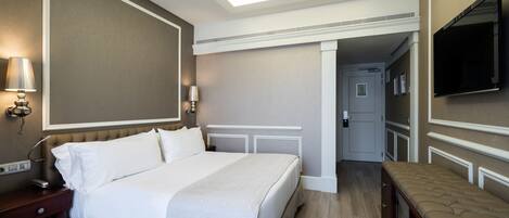 Ein Hotelzimmer mit einem großen Bett, Nachttischlampen, einem Flachbildfernseher und einer Bank.