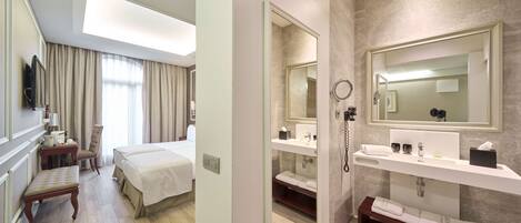 A hotel room with a bed, a desk, a chair, a vanity with a mirror, and a shower area.