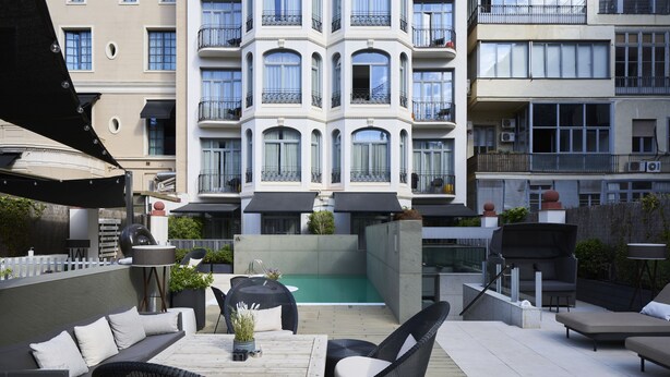 Un patio en la azotea con mobiliario exterior, una piscina y vistas a un edificio de varios pisos con balcones.