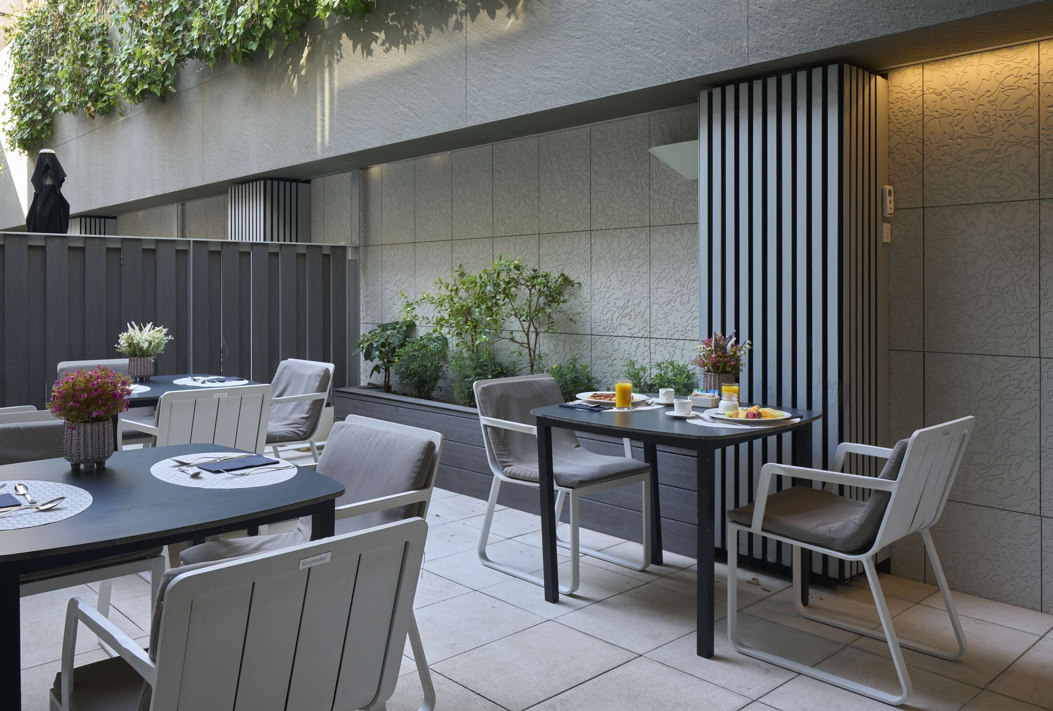 An outdoor dining area with tables and chairs, a potted plant, and a wall with vertical lines.