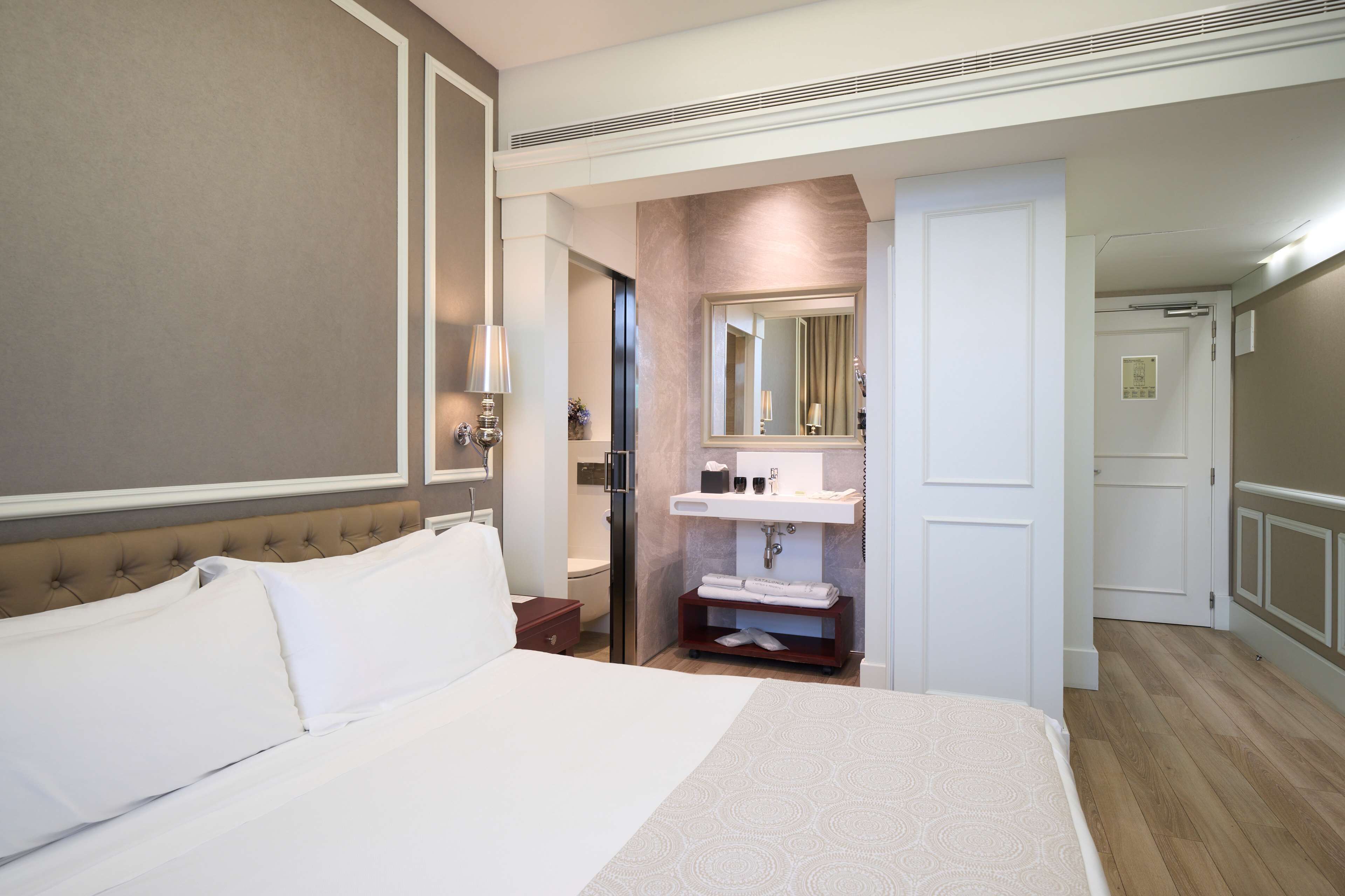 Ein Hotelzimmer mit einem großen Bett, einem Badezimmer mit Waschbecken und Spiegel sowie einer Tür zu einem weiteren Raum.