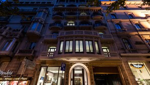 Fachada de un hotel histórico con balcones ornamentales, una entrada imponente y un letrero que indica una tienda Menkes cercana.