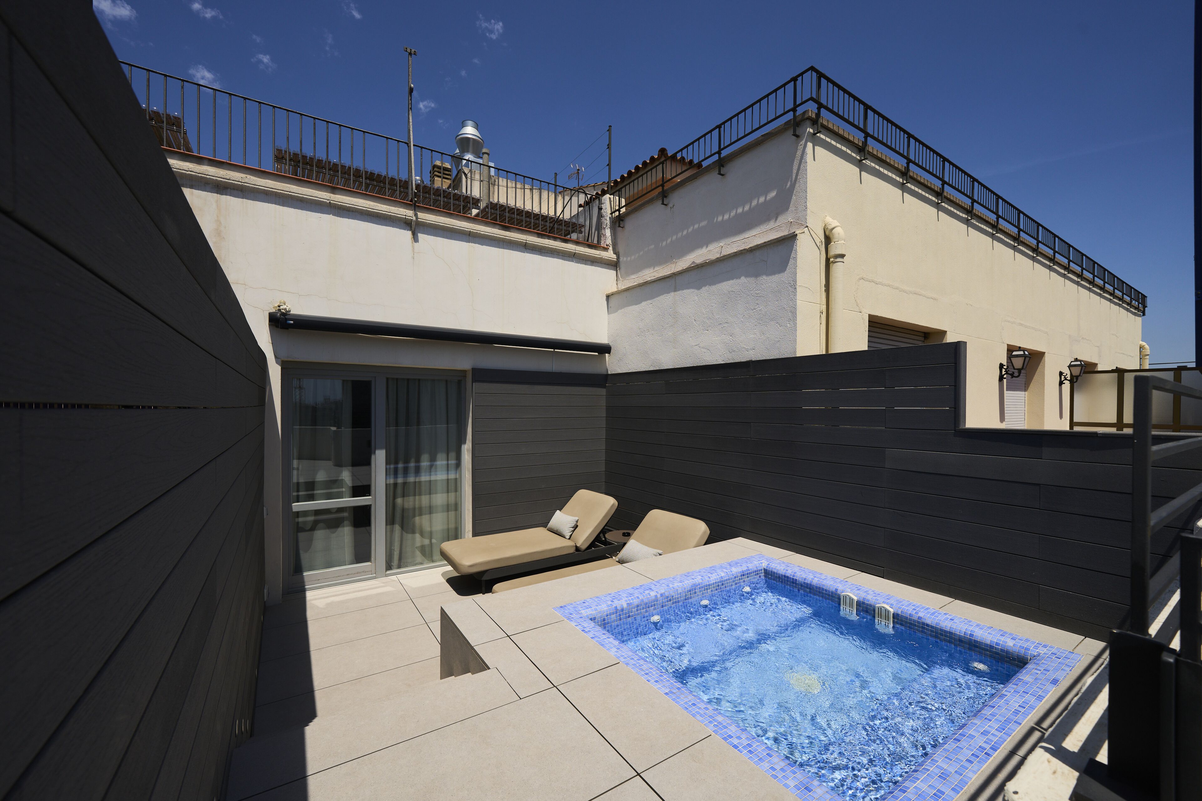 Área de piscina no terraço com hidromassagem, espreguiçadeiras e porta de vidro que dá para uma varanda.