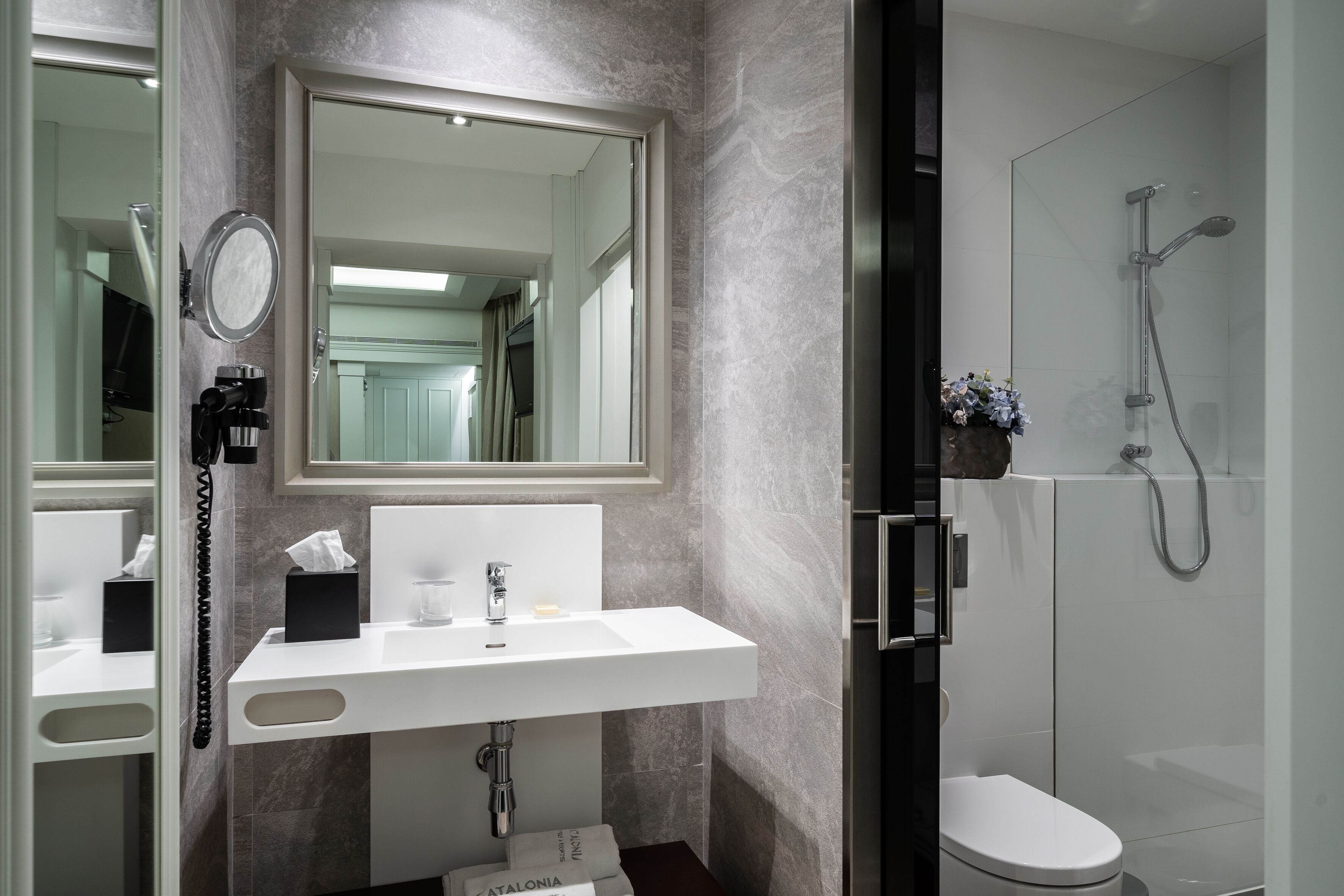 Un baño moderno con un lavamanos blanco, un espejo, un cabezal de ducha de mano y un inodoro.