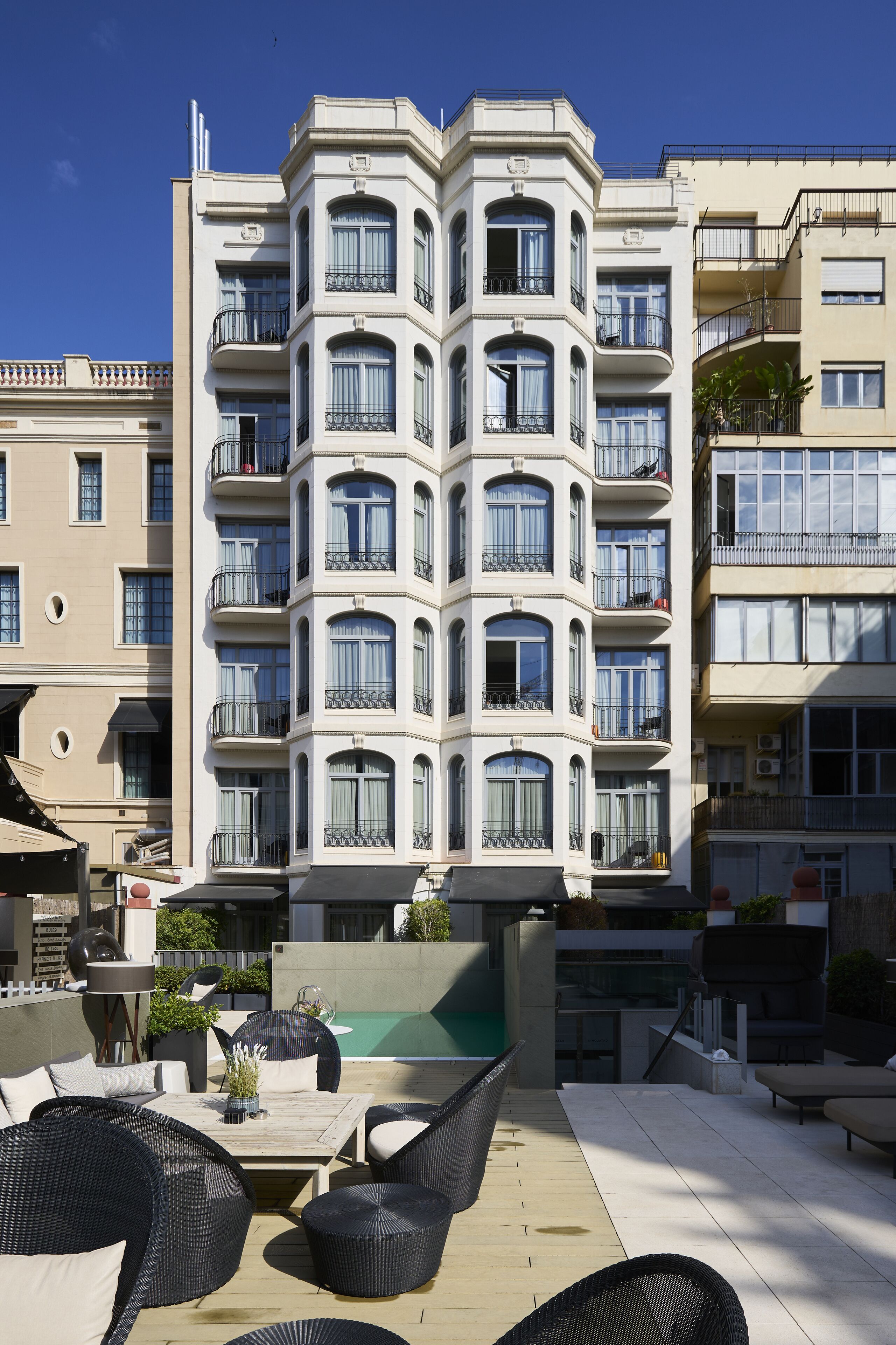 A multi-story building with balconies, a rooftop patio with outdoor furniture, and a swimming pool.