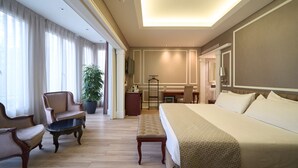 Habitación de hotel con una cama grande, dos sillones, una mesita, una planta en maceta y un escritorio con silla.