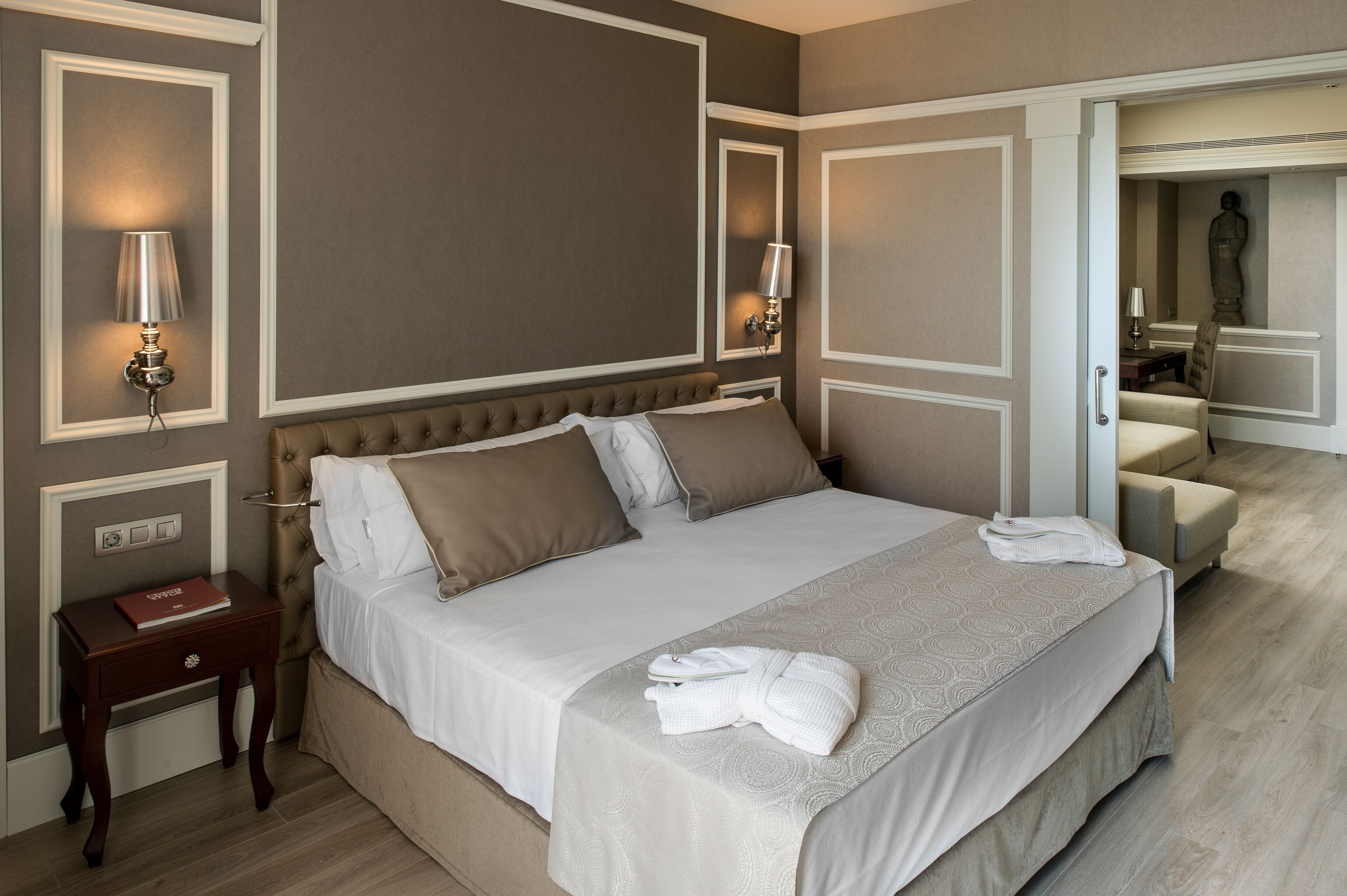 Hotellihuone, jossa on suuri sänky, kaksi yöpöytävalaisinta, yöpöytä ja tuoli.