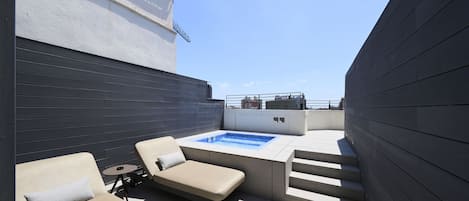 Un patio al aire libre con un jacuzzi, dos sillones de descanso y una mesita.