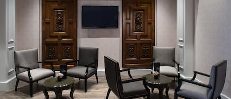 A room with four upholstered chairs, two small round tables, and two large wooden doors with intricate carvings.