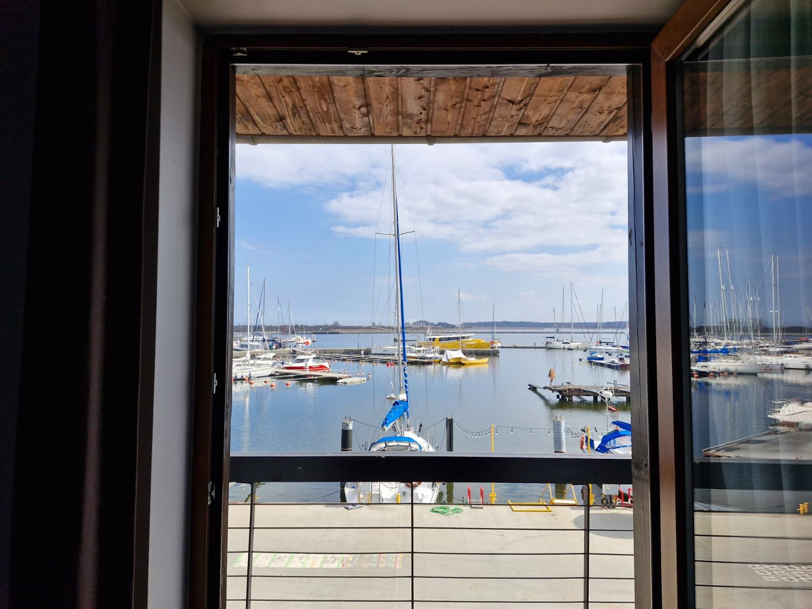 A view of a marina with multiple boats docked, a clear sky, and a wooden ceiling above the window.