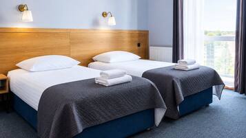 A hotel room with two beds, a wooden headboard, a nightstand, and a window with curtains.