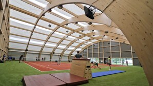 Instal·lació esportiva interior amb pista de tennis, paret d'escalada i zona amb protecció de goma.