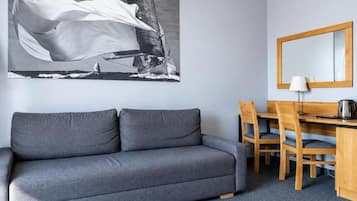 Ein Zimmer mit einer grauen Couch, einem Holztisch mit Stühlen, einem großen gerahmten Bild an der Wand und einem Spiegel über dem Tisch.