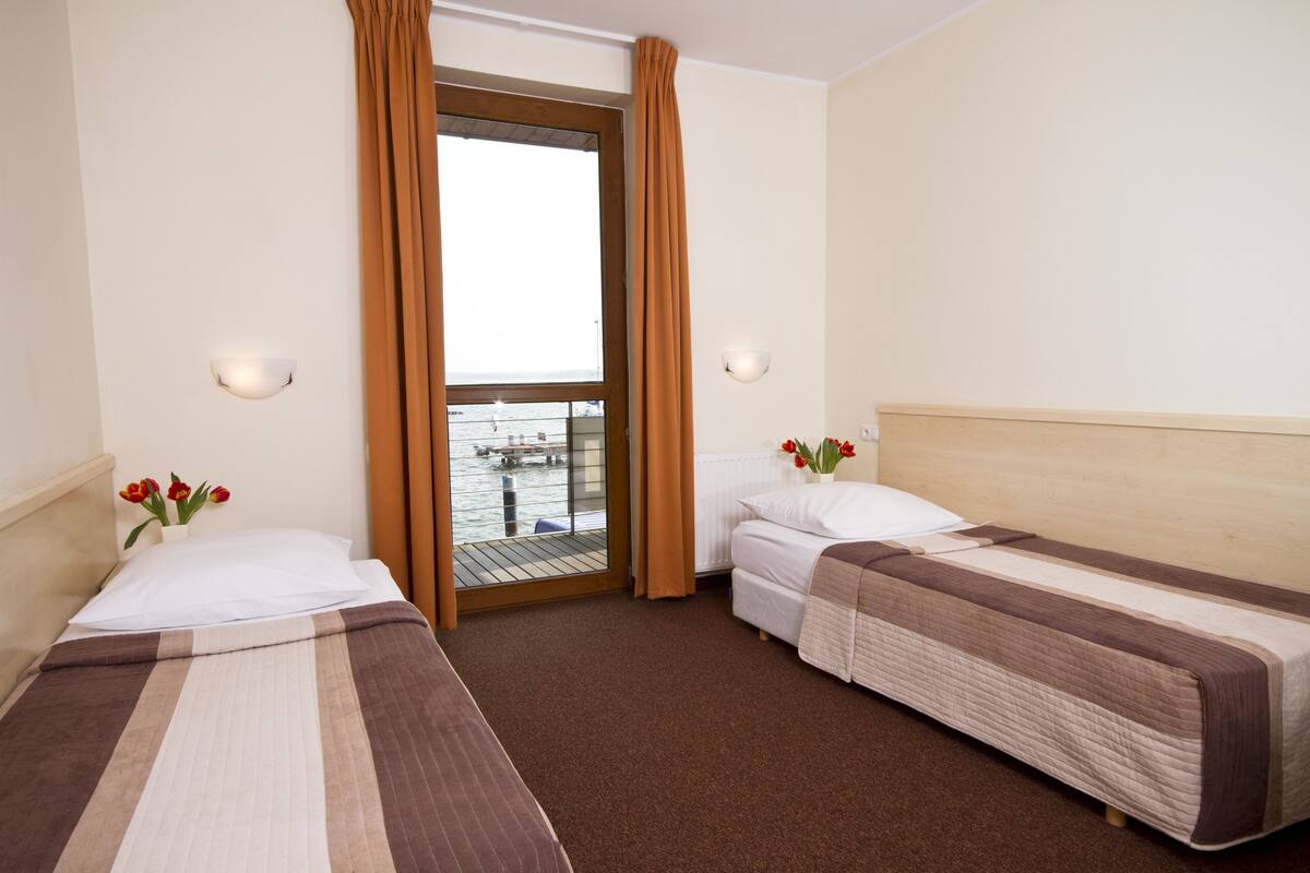 Habitación de hotel con dos camas, un balcón con vista al mar y una ventana con cortinas.