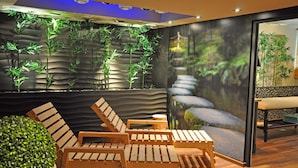 A modern relaxation area with wooden lounge chairs, a small table, and a wall-mounted aquarium with bamboo plants. - Hotel Orle (Gdansk)