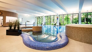 A modern indoor swimming pool with clear glass walls, a tiled floor, and a seating area with a plant. - Hotel Orle (Gdansk)