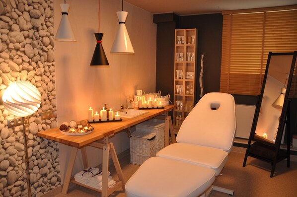 Un cuarto de spa con una mesa de madera, velas, una silla de masaje blanca y un estante con artículos de aseo.