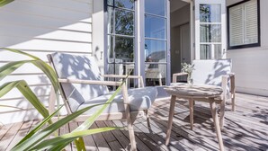 A wooden deck with a white chair and a small table, a glass door leading to a covered area, and a window with shutters. - The Martinborough Hotel (Martinborough)