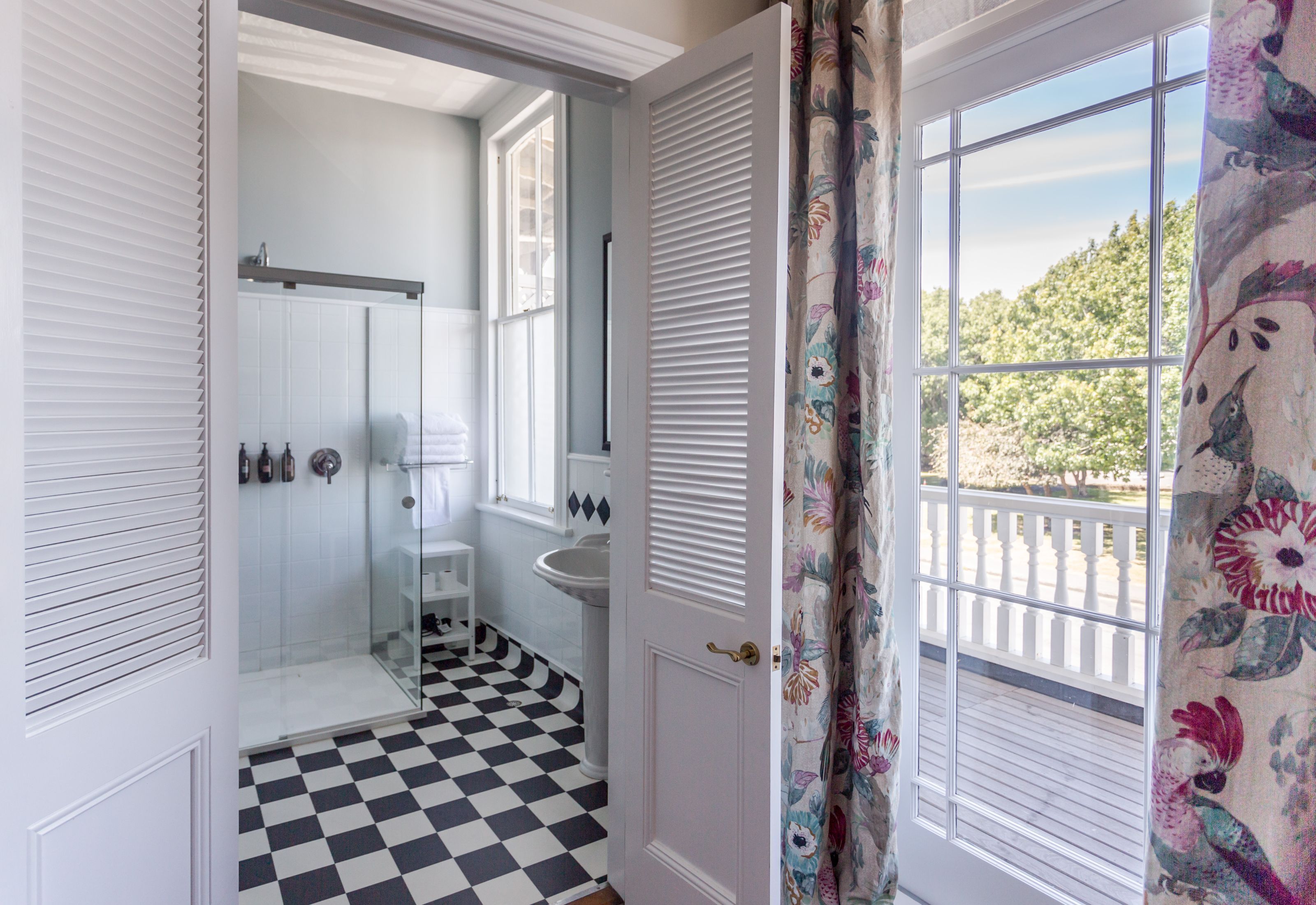 A bathroom with a checkered floor, a glass shower enclosure, a sink, and a window with a view of trees.