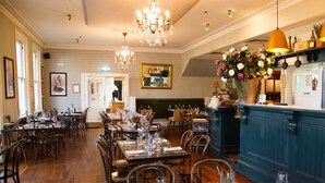 A restaurant with wooden tables and chairs, a bar area, and a chandelier. - The Martinborough Hotel (Martinborough)