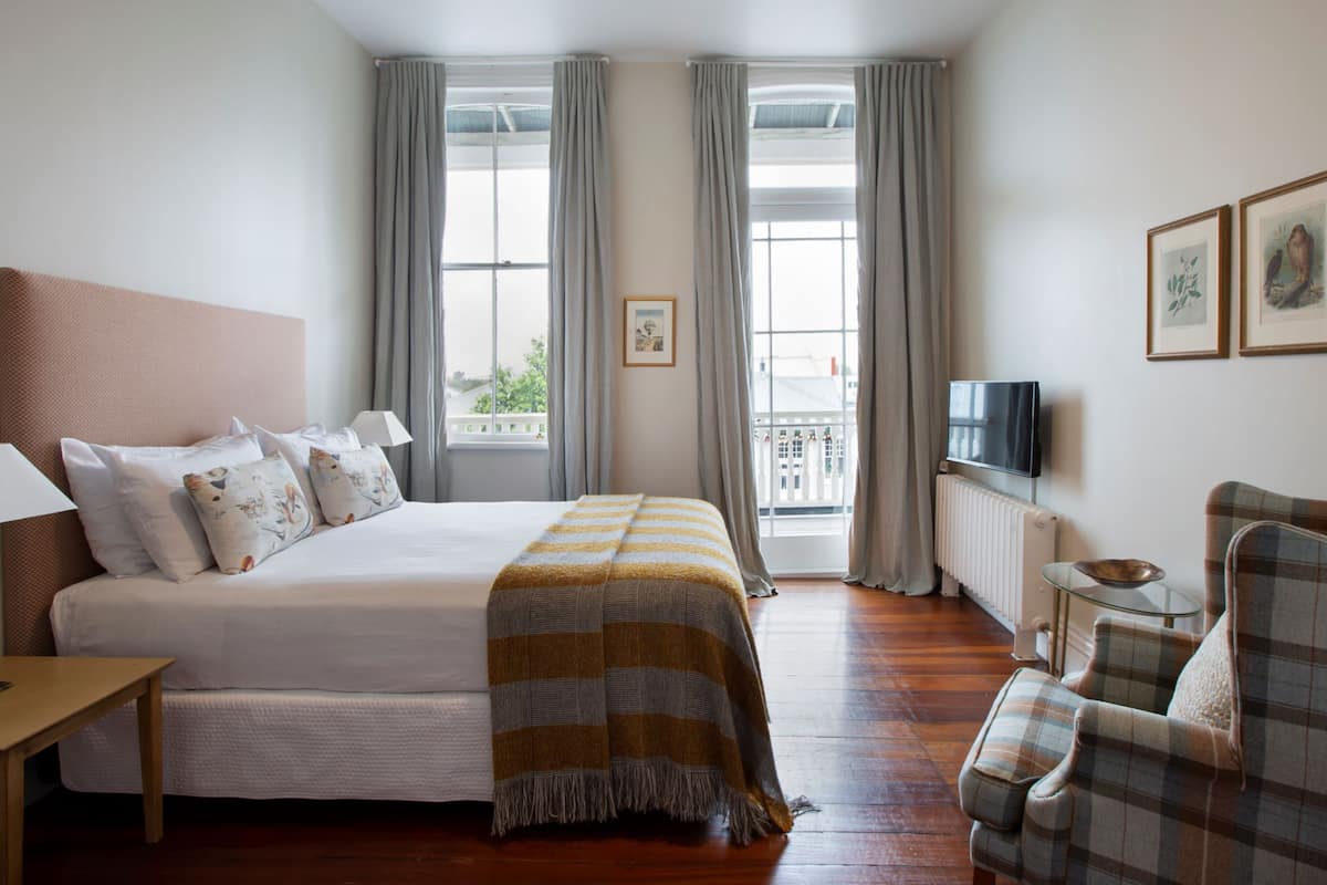 A hotel room with a large bed, a television, a chair, and a balcony with curtains.