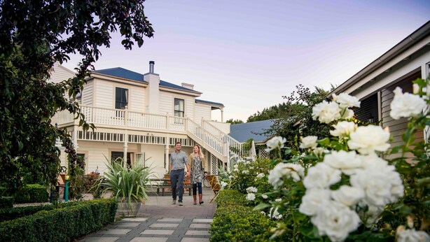 A pathway leading to a house with a balcony, surrounded by greenery and white flowers. - The Martinborough Hotel (Martinborough)
