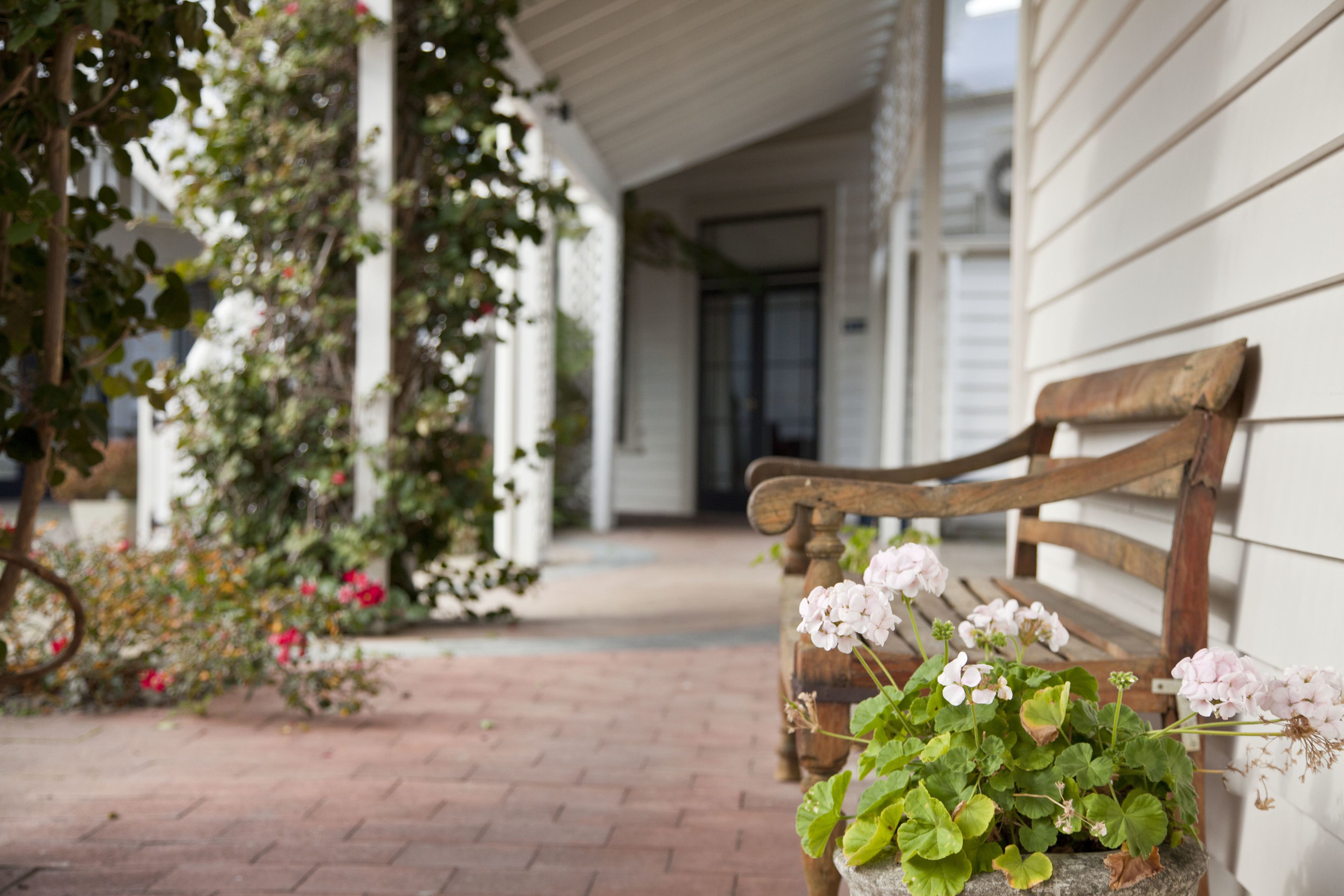 A wooden bench with a potted plant beside a white building.