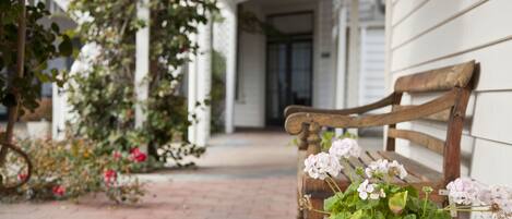 A wooden bench with a potted plant beside a white building.