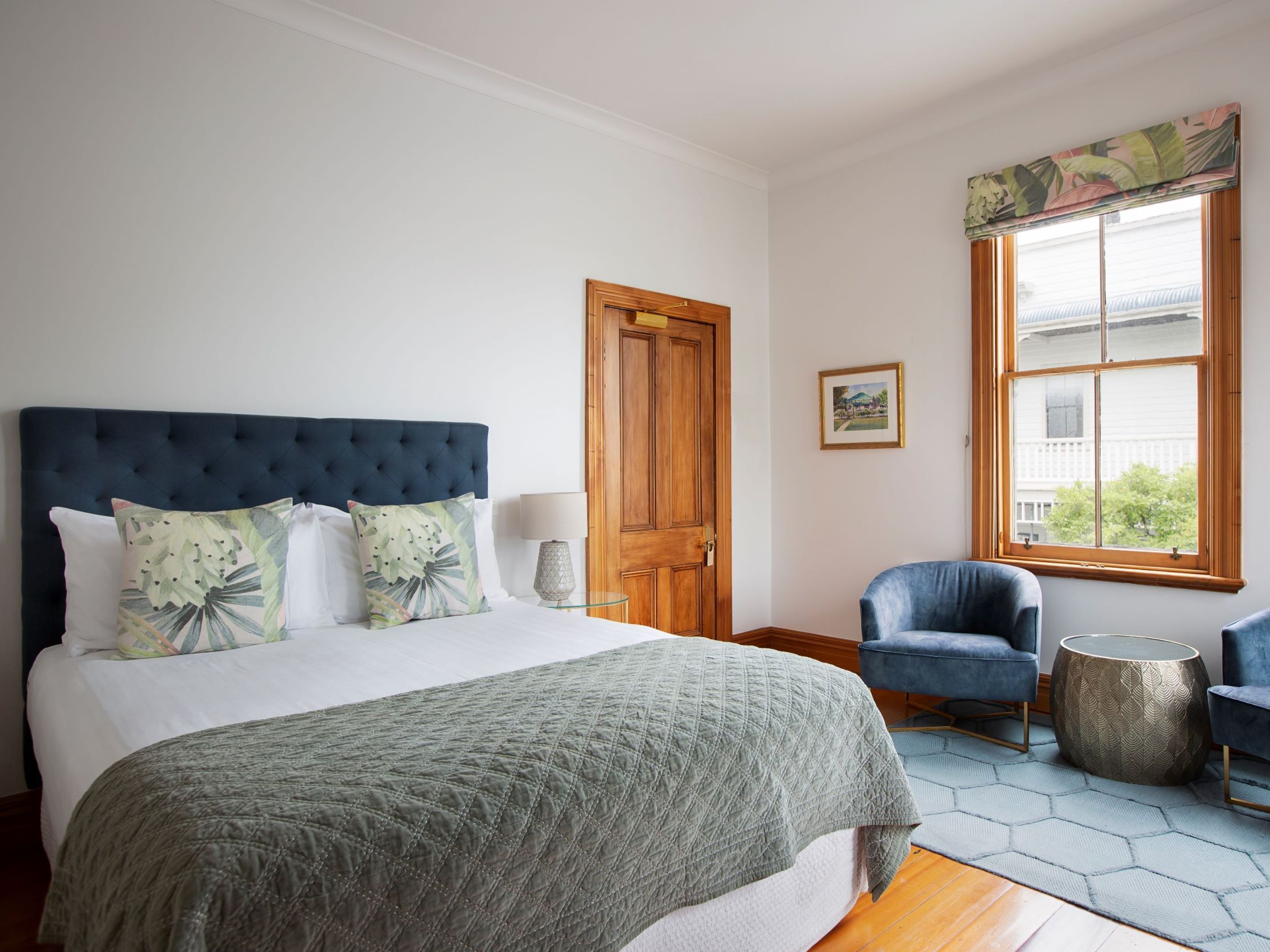 Een slaapkamer met een groot bed, een houten deur, een raam met uitzicht en twee stoelen.