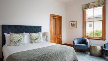 Een slaapkamer met een groot bed, een houten deur, een raam met uitzicht en twee stoelen.