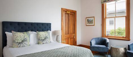 Un dormitorio con una cama grande, una puerta de madera, una ventana con vistas y dos sillas.