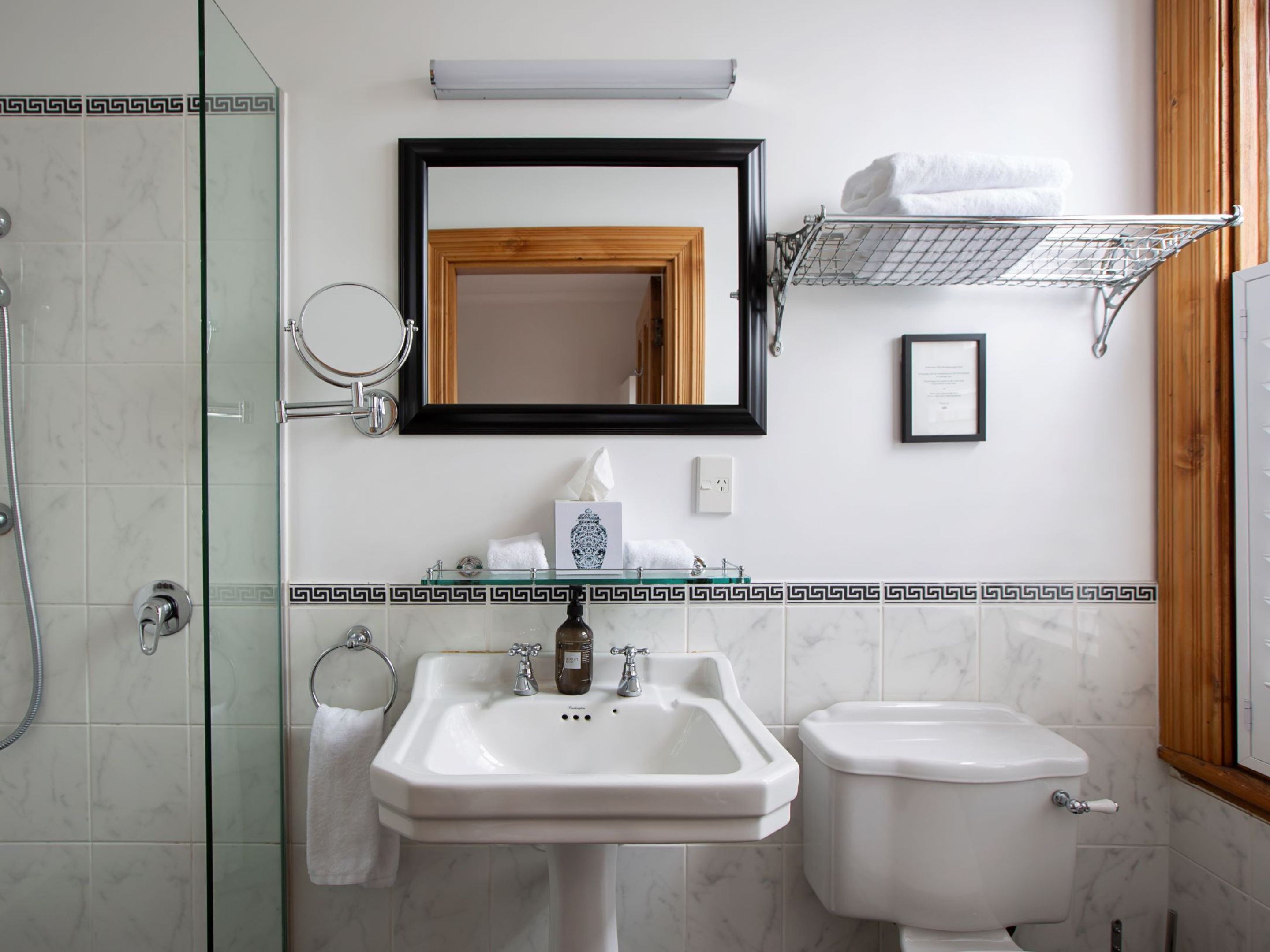 A bathroom with a glass shower enclosure, a white sink with a mirror above it, a toilet, and a towel rack with towels.