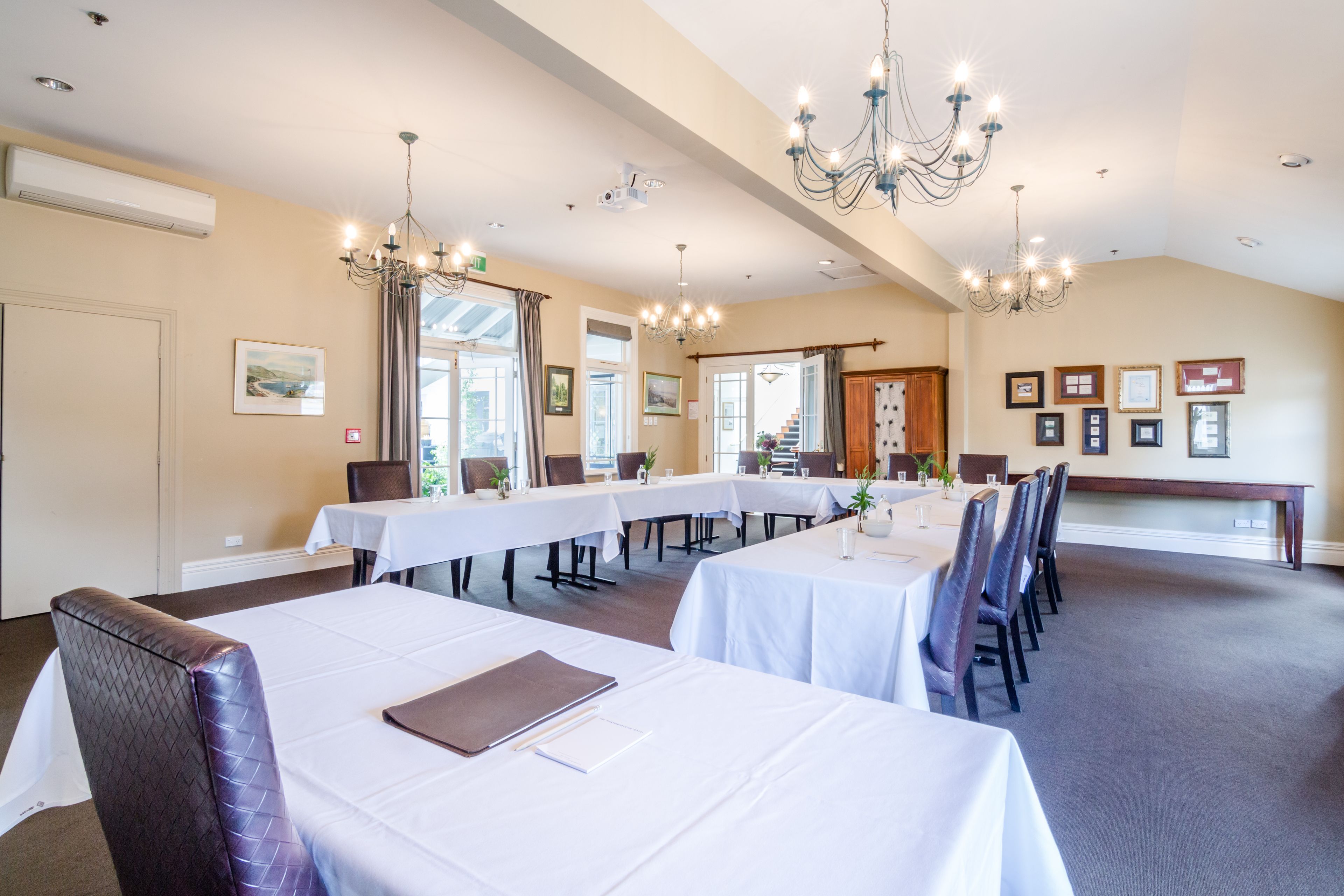 Une grande salle à manger avec de nombreuses tables et chaises, des lustres et des tableaux encadrés aux murs.