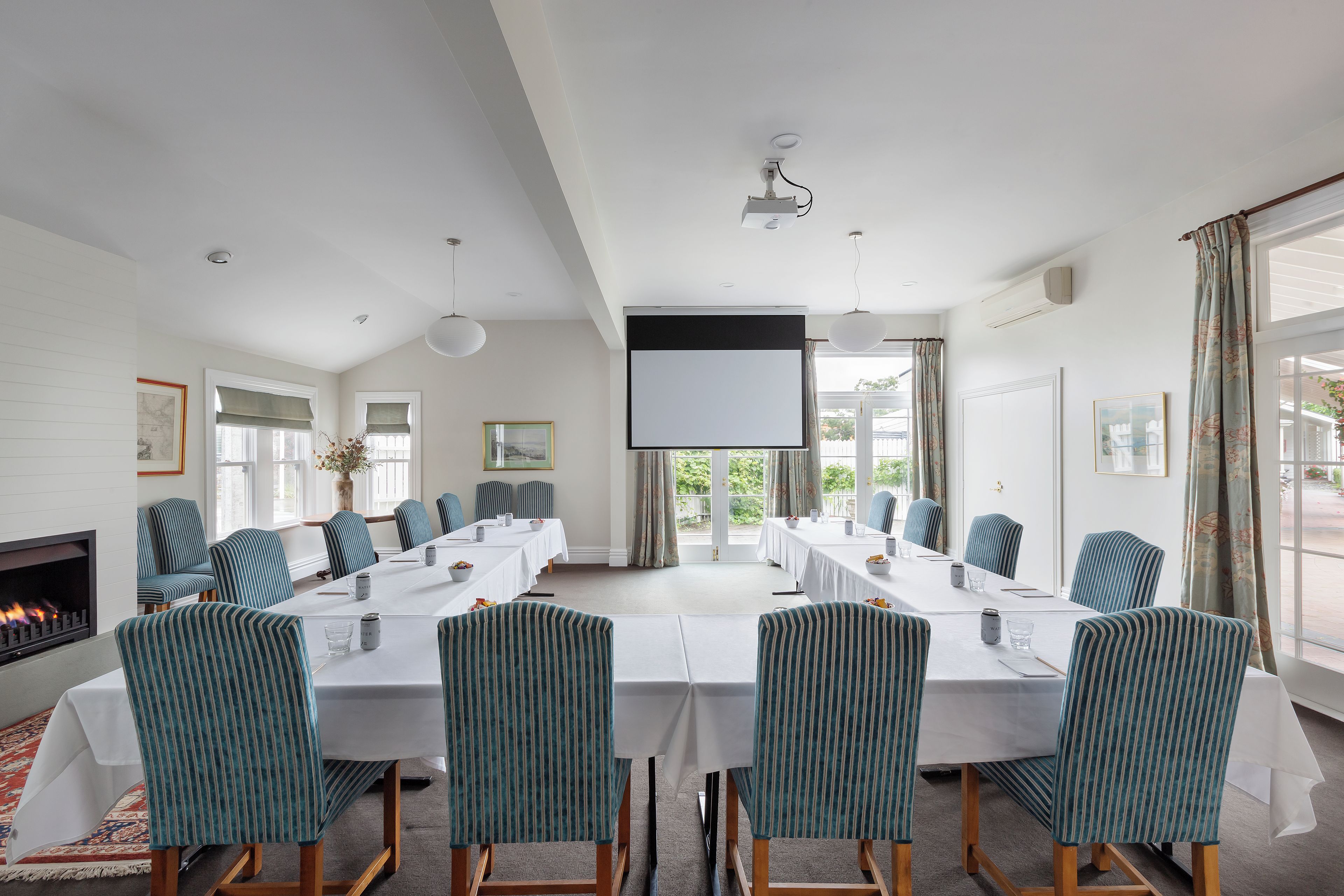 A conference room with a long table, chairs, a projector screen, and a fireplace.