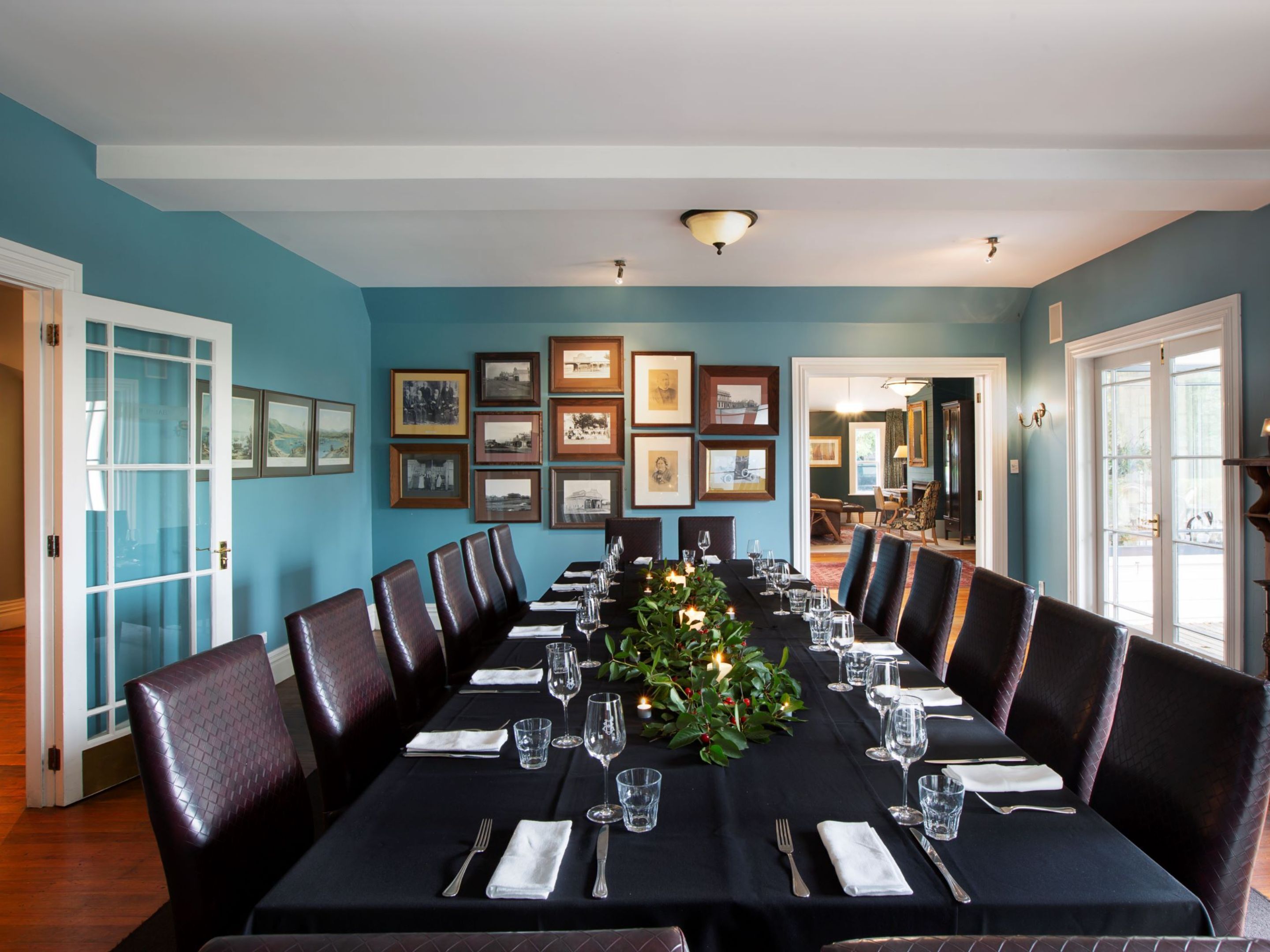 A dining area with a long table set for a meal, framed pictures on the wall, and a view into another room.