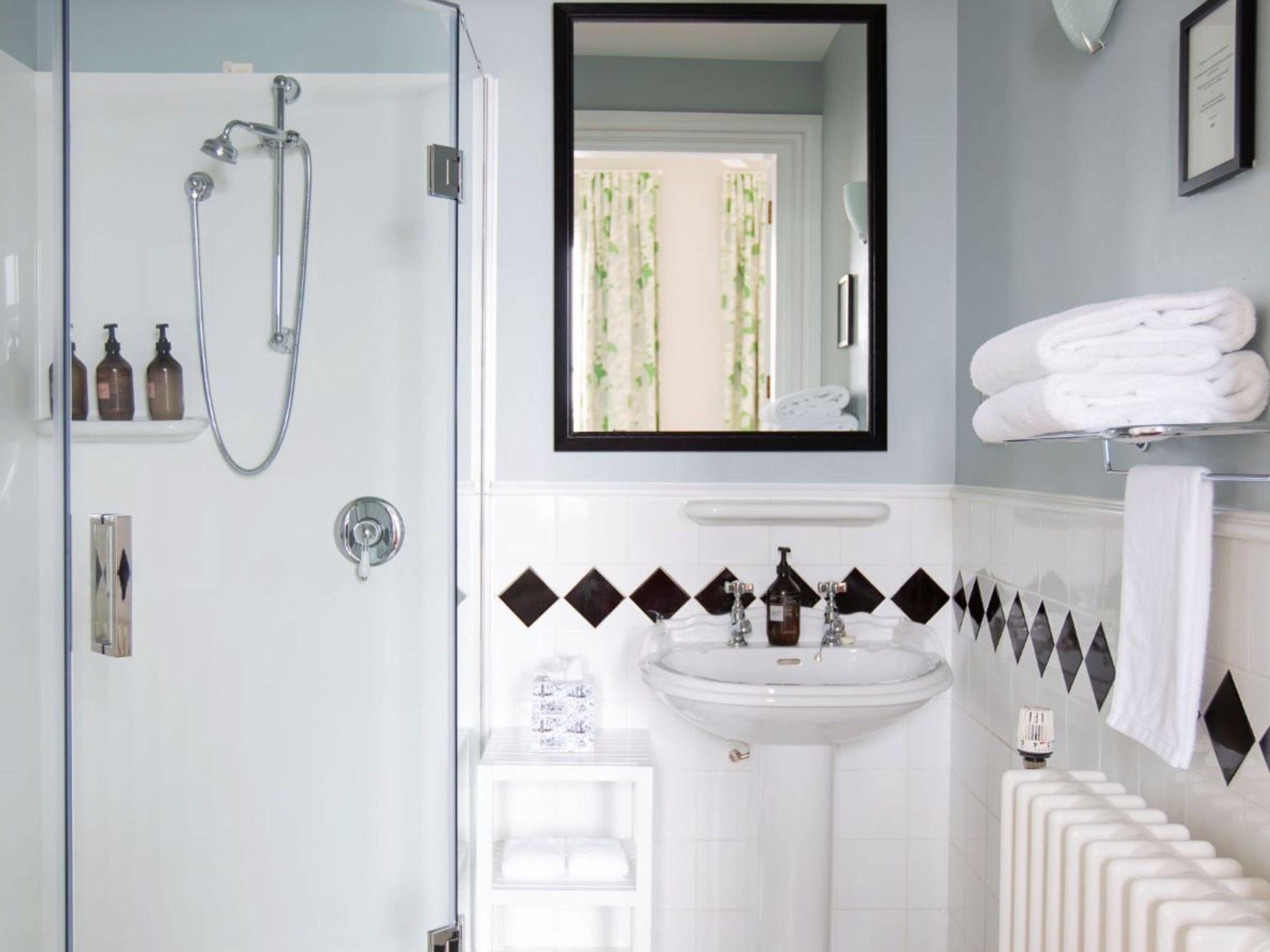 Een badkamer met een glazen douchecabine, een wit wastafelmeubel met zwart, diamantvormig betegelde details, en een spiegel boven het wastafelmeubel.