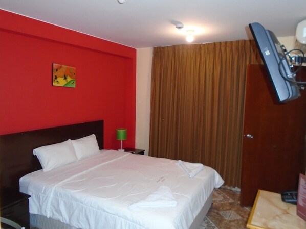 Habitación de hotel con una cama grande, una mesita de noche, una lámpara verde, un cuadro en la pared y una cortina.