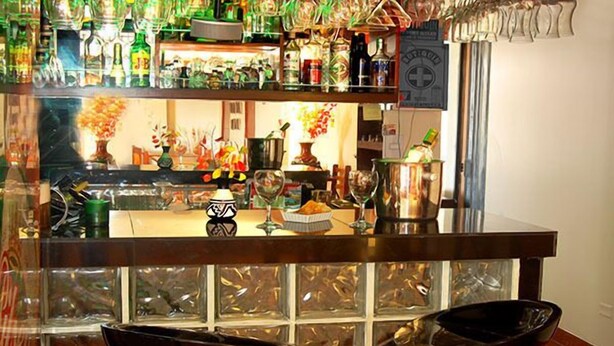 A bar area with shelves of bottles and glasses, a counter with a vase of flowers, and a decorative wall with a grid pattern. - Royal Inca Hotel (Lima)