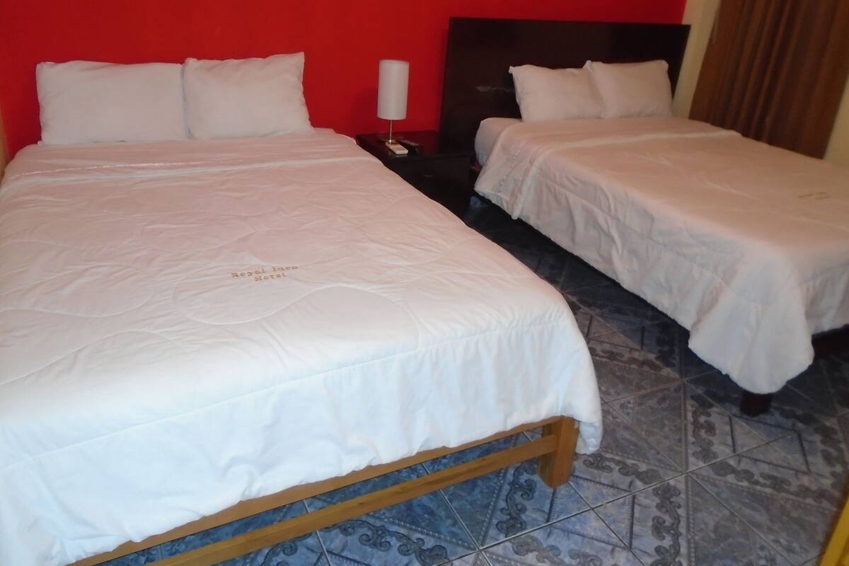 A hotel room with two beds, a nightstand, and a red wall.