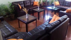 A modern living room with black leather sofas, glass coffee tables, and orange cushions. There are several potted plants around the room. - Royal Inca Hotel (Lima)