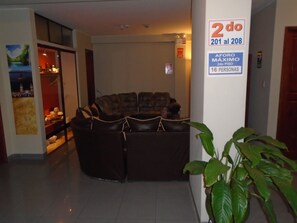 Un hall con zona de estar, un cartel con los números de las habitaciones y un aviso sobre la ocupación máxima.