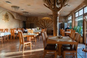 A restaurant with wooden tables and chairs, a large tree sculpture centerpiece, and a view of the outdoors through large windows.