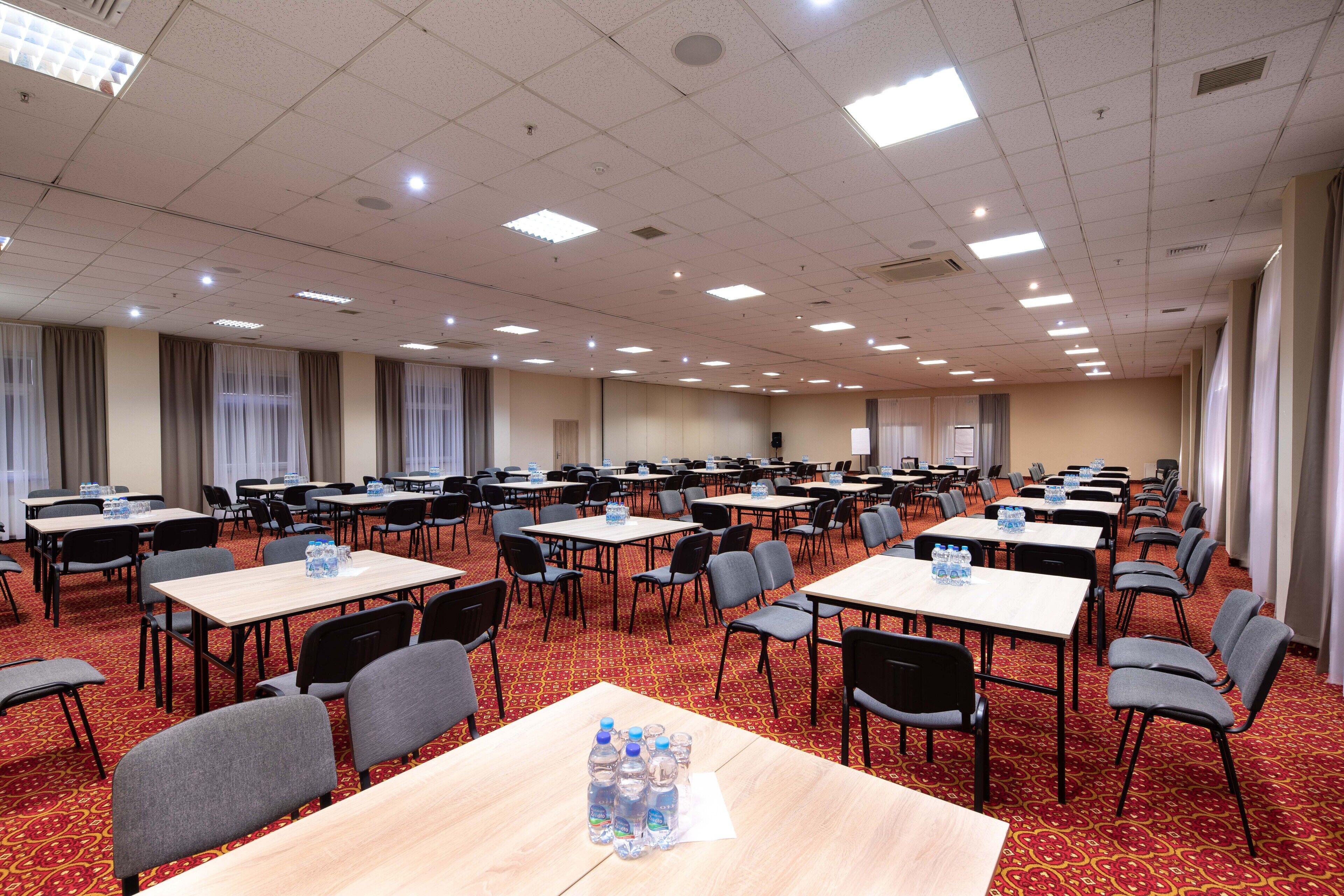 A conference room with multiple tables and chairs, equipped with water bottles and a projector screen.