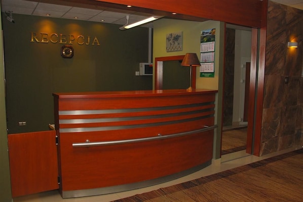 A reception desk with a wooden finish, a clock, and a calendar on the wall. - Ośrodek hotelowy Optima (Kraków)