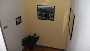 Um corredor com uma fotografia emoldurada na parede, um vaso de planta e uma placa acima da fotografia.