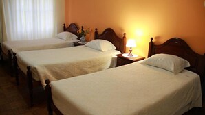 Quarto de hotel com três camas de solteiro, cabeceiras de madeira e uma mesa de cabeceira com abajur.