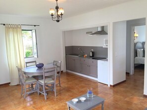 A compact kitchen with grey cabinets, a stainless steel range hood, and a white microwave. There's a dining area with a round table and chairs, and a small table with candles.